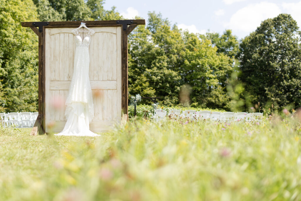 Photo of wedding dress hanging on wooden doors in an open field