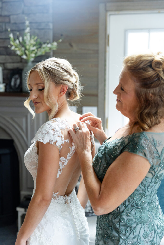 Mother of the bride helps button the back of the bride's dress. 