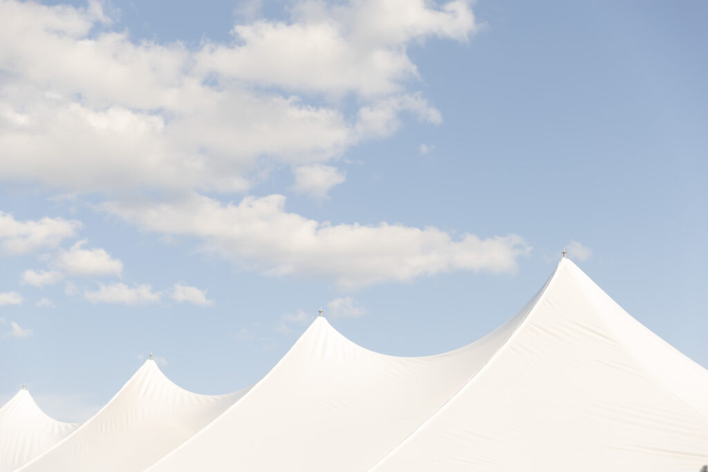 Photo of the top of a reception tent on a cloudy, blue skied August day. 