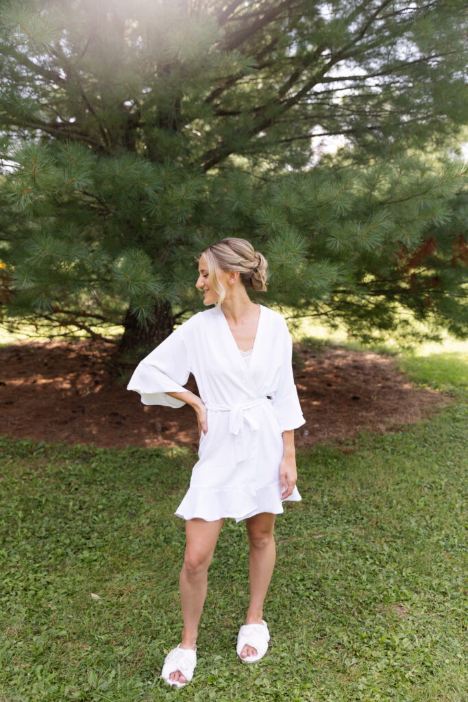 Bride smiling over her shoulder at the ground in her robe and slippers. 